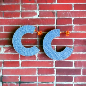 May include: Two large, blue, denim-like hoop earrings with gold-colored clasps. The earrings are in the shape of the letter "C".