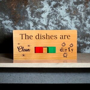Puede incluir: Un letrero de madera con el texto "The dishes are" y un indicador deslizante que dice "Clean" en un lado y "Dirty" en el otro.
