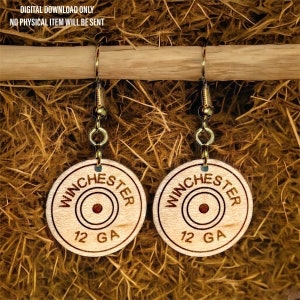 May include: A pair of wooden earrings with a gold-colored hook. The earrings are round and feature a wood-burned design of a Winchester 12 GA shotgun shell.