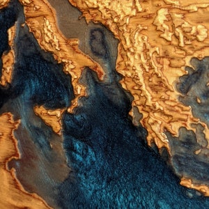 K&ouml;nnte beinhalten: Eine Holzkarte des Mittelmeers mit einer blauen Harz-Einlage. Die Karte ist in einem dunklen Holzrahmen gerahmt und tr&auml;gt die Inschrift "MEDITERRANE" am unteren Rand.