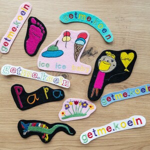 Könnte beinhalten: Eine Sammlung bunter Filzpatches mit gestickten Wörtern und Designs. Die Patches beinhalten die Wörter "getme.koeln", "Papa", "ice ice baby" und "Love". Außerdem gibt es einen Patch mit einer Cartoon-Zeichnung einer Person und einen Patch mit einer Cartoon-Zeichnung einer Eidechse.