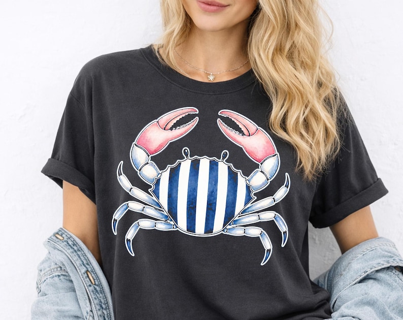 May include: Dark gray t-shirt featuring a blue crab illustration with pink claws and a striped body. The crab design is centered on the shirt. The shirt has short sleeves and a relaxed fit.