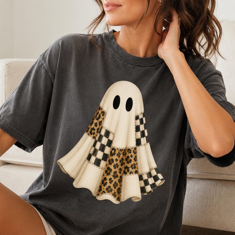 Puede incluir: Una camiseta de manga corta gris carb&oacute;n con un gr&aacute;fico central de un fantasma. El fantasma est&aacute; compuesto por varias secciones de patchwork, alternando entre crema s&oacute;lido, patrones de cuadros blancos y negros y estampados de leopardo.