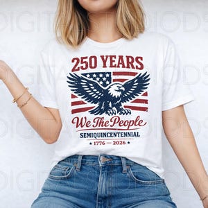 May include: White t-shirt with a patriotic design. The graphic features an American flag, an eagle, and the text "250 YEARS We The People SEMIQUINCENTENNIAL 1776-2026". The shirt is worn with blue jeans.