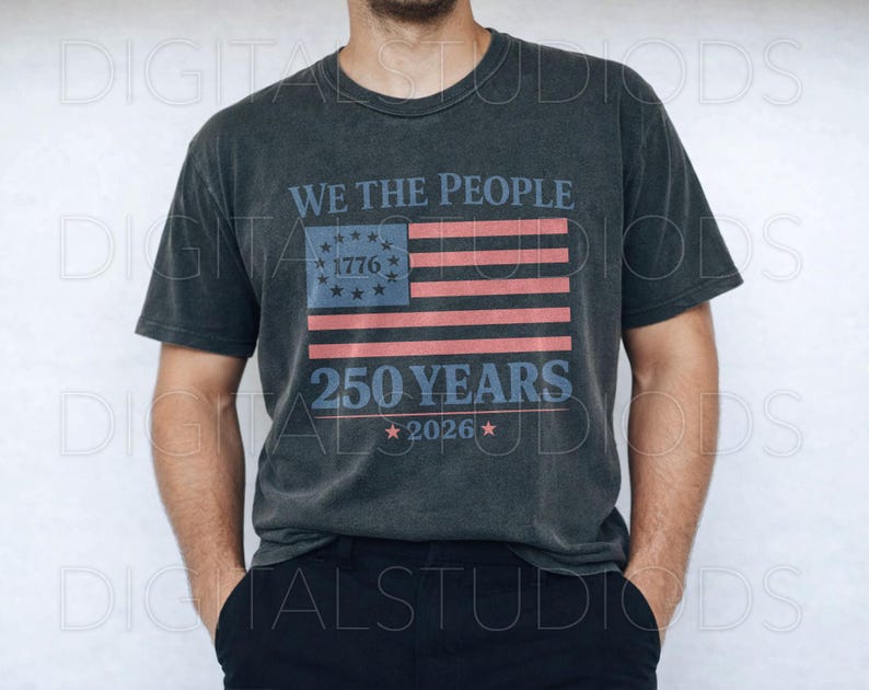 May include: Dark gray t-shirt featuring the text "WE THE PEOPLE" above a stylized American flag design with the text "1776" and "250 YEARS 2026". The shirt has a vintage, worn look.