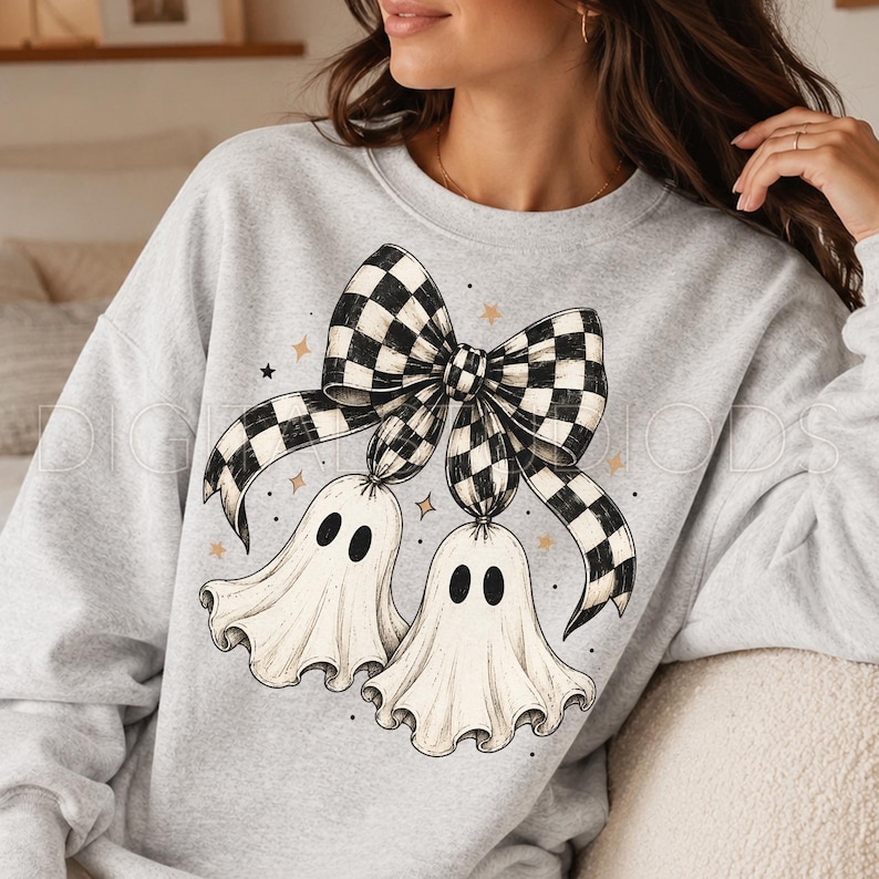 Op de afbeelding: Een lichtgrijs sweatshirt met ronde hals en een grafische print van twee gebroken witte spoken die aan een grote zwart-wit geblokte strik hangen. Het ontwerp bevat kleine gouden steraccenten en zwarte stippen rond de illustratie.