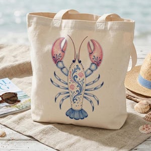 May include: A cream-colored tote bag featuring a detailed illustration of a lobster. The lobster design incorporates pink, blue, and white accents. The bag has two handles and is made of a sturdy fabric, perfect for carrying beach essentials.