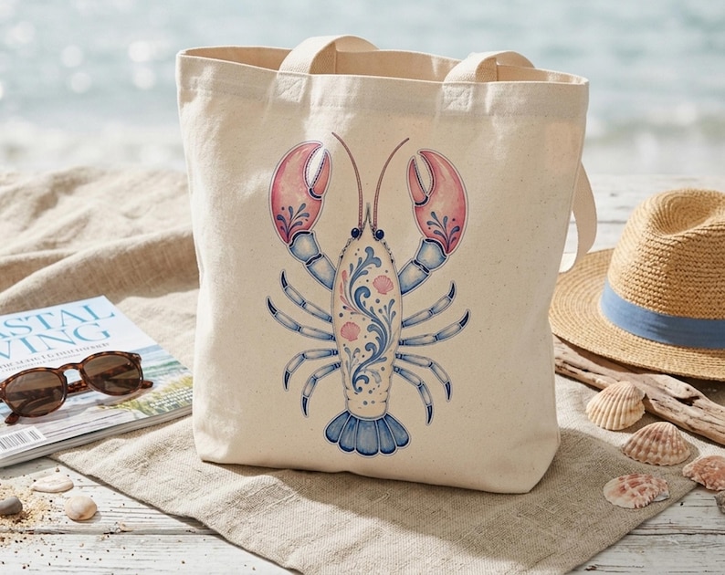 May include: A cream-colored tote bag featuring a detailed illustration of a lobster. The lobster design incorporates pink, blue, and white accents. The bag has two handles and is made of a sturdy fabric, perfect for carrying beach essentials.