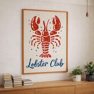 May include: A framed print featuring a red lobster illustration with the words "Lobster Club" in blue script. The artwork is set against a cream background and framed in a light brown wooden frame. The print is displayed on a wooden cabinet.