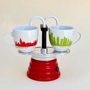 May include: A white ceramic mug with a black handle and the text "But First, Coffee" in a bold, black font. The mug is sitting on a wooden surface. The mug is approximately 4 inches tall.