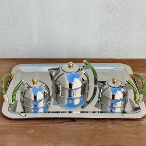 Può includere: Un set di tre tazze in ceramica con una glassa screziata color crema. Ogni tazza presenta un design dipinto a mano diverso: una foglia blu e verde, un fiore giallo e una bacca rossa. Le tazze hanno un design semplice e moderno.