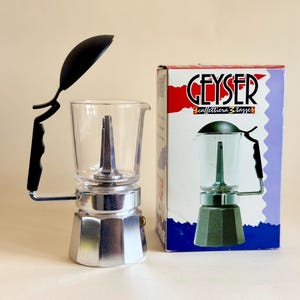 Könnte beinhalten: Ein Set aus drei Keramikbechern mit gesprenkelter, matter Oberfläche. Die Becher sind in Creme-, Hellgrau- und Dunkelgrautönen gehalten. Jeder Becher hat ein schlichtes, minimalistisches Design und einen abgerundeten Henkel.