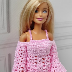 Op de afbeelding: Een roze gebreide off-shoulder top en rok set voor een pop. De top heeft wijde mouwen en de rok is een minirok.