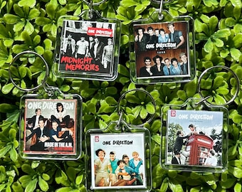 May include: Five clear plastic keychains with different One Direction album covers. The keychains feature the albums "Midnight Memories", "Four", "Made in the A.M.", "Take Me Home", and "Up All Night".