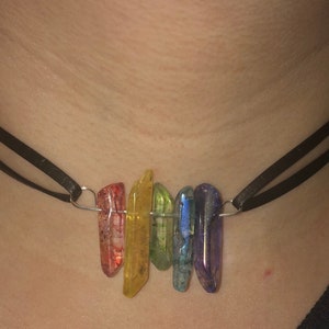 May include: A rainbow crystal choker necklace with a black leather cord. The crystals are in the order of red, orange, yellow, green, blue, and purple.