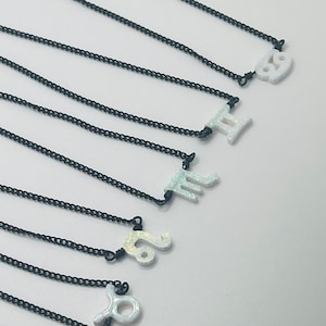May include: A set of ten necklaces with black chains and white opal zodiac signs. The signs are: Libra, Taurus, Leo, Scorpio, Pisces, Gemini, Cancer, Virgo, Sagittarius, and Capricorn.