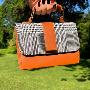 May include: A small brown and black checkered handbag with a gold clasp and a brown leather strap.