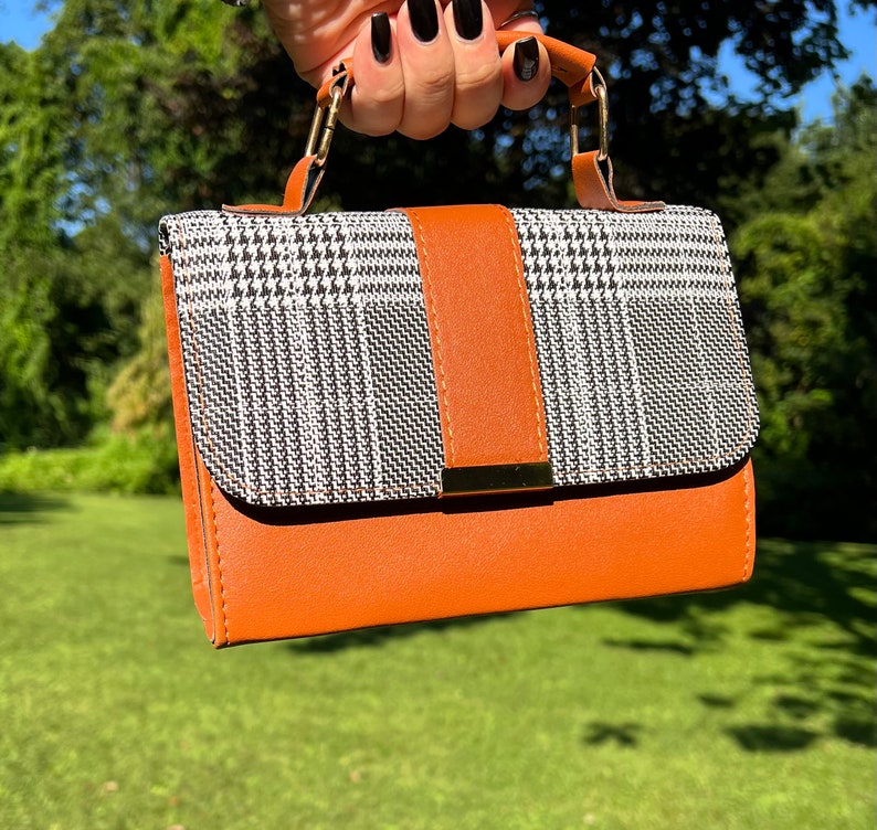 May include: A small brown and black checkered handbag with a gold clasp and a brown leather strap.