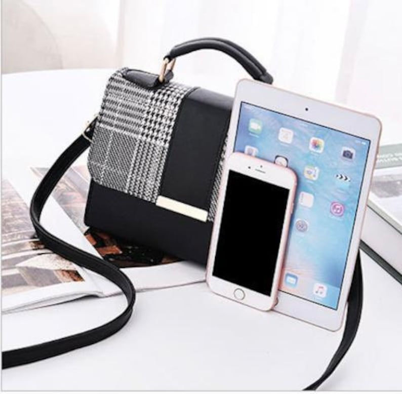 May include: A black and white plaid handbag with a black leather flap and gold hardware. The bag has a top handle and a long shoulder strap. A tablet and a smartphone are placed next to the bag.