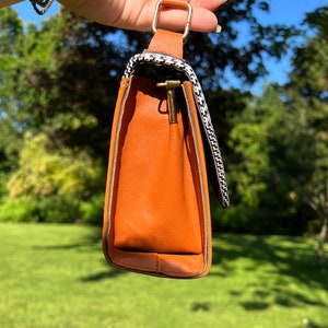 May include: A small brown handbag with a black and white checkered pattern on the flap. The bag has a gold metal clasp and a gold chain strap.