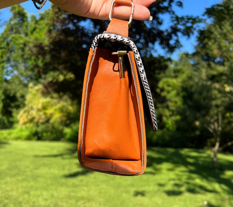May include: A small brown handbag with a black and white checkered pattern on the flap. The bag has a gold metal clasp and a gold chain strap.