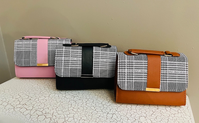 May include: Three small handbags with a black and white plaid pattern. The handbags have a contrasting colored flap and strap. The handbags are pink, black, and brown.