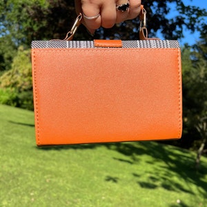 May include: A small orange handbag with a black and white patterned top flap and a silver handle.