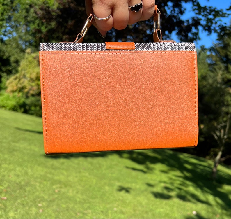 May include: A small orange handbag with a black and white patterned top flap and a silver handle.