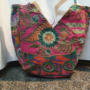 May include: A pink tote bag with colorful embroidered floral designs. The bag has a white canvas strap.