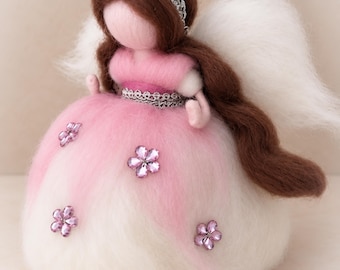 May include: A needle-felted angel figurine with long brown hair, a silver headband, and white wings. The figure wears a pink and white dress adorned with small, sparkling pink flower-shaped embellishments and a silver trim around the waist.