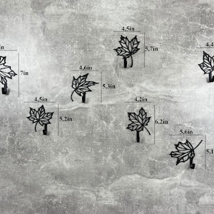May include: Six black metal leaf-shaped hooks with measurements in inches. The hooks are designed to look like maple leaves.