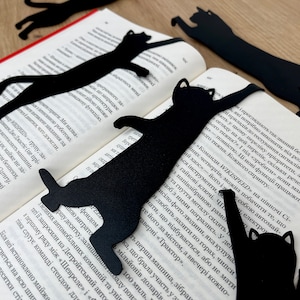 Pu&ograve; includere: Cinque segnalibri di metallo nero a forma di gatto su un libro. I segnalibri hanno la forma di un gatto in diverse pose.