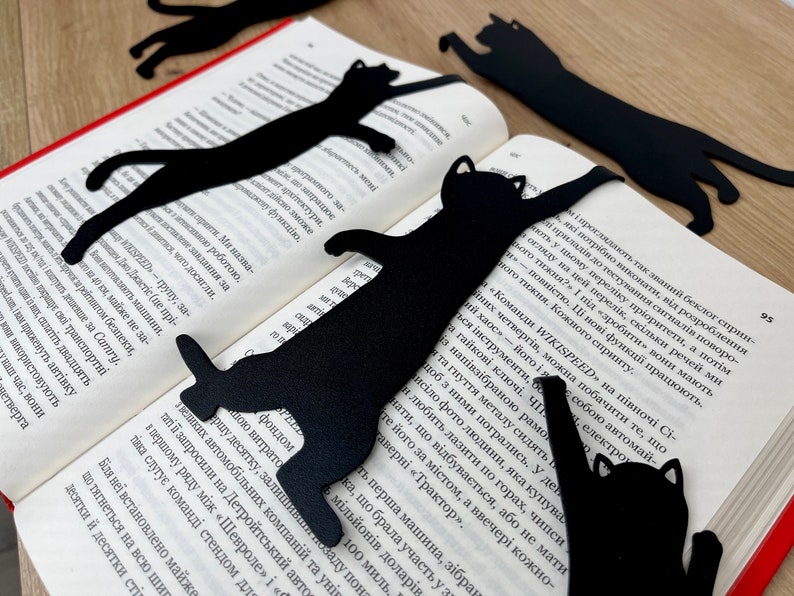 Pu&ograve; includere: Cinque segnalibri di metallo nero a forma di gatto su un libro. I segnalibri hanno la forma di un gatto in diverse pose.