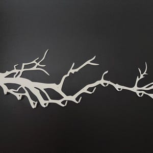May include: A white metal wall art piece in the shape of a tree branch, with multiple offshoots and a textured surface. The branch is mounted on a black background, creating a striking contrast. This decorative piece is ideal for adding a natural element to any room.