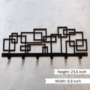 Puede incluir: Perchero de pared de metal negro con un dise&ntilde;o geom&eacute;trico. Presenta una serie de cuadrados y rect&aacute;ngulos entrelazados. El perchero tiene seis ganchos y mide 60 cm de alto y 22,4 cm de ancho.