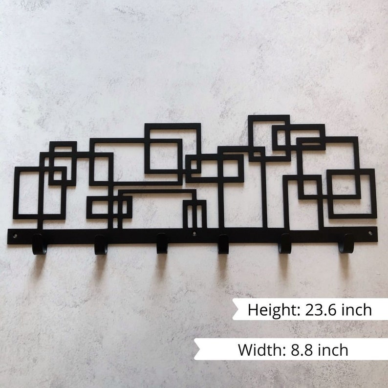 Puede incluir: Perchero de pared de metal negro con un dise&ntilde;o geom&eacute;trico. Presenta una serie de cuadrados y rect&aacute;ngulos entrelazados. El perchero tiene seis ganchos y mide 60 cm de alto y 22,4 cm de ancho.
