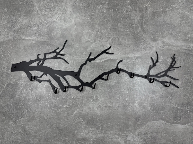 May include: Black metal wall-mounted coat rack in the shape of a tree branch. The rack has multiple hooks for hanging coats, hats, or other items. The design is a silhouette of a tree branch with a matte finish.