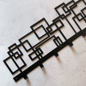 Puede incluir: Perchero de pared de metal negro con un dise&ntilde;o geom&eacute;trico y cinco ganchos.