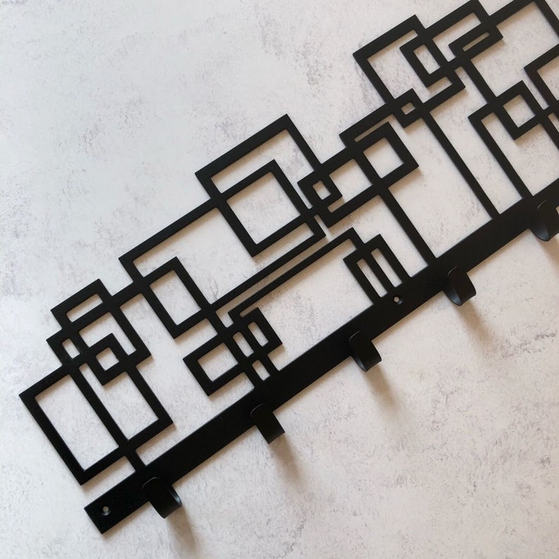 Puede incluir: Perchero de pared de metal negro con un dise&ntilde;o geom&eacute;trico y cinco ganchos.