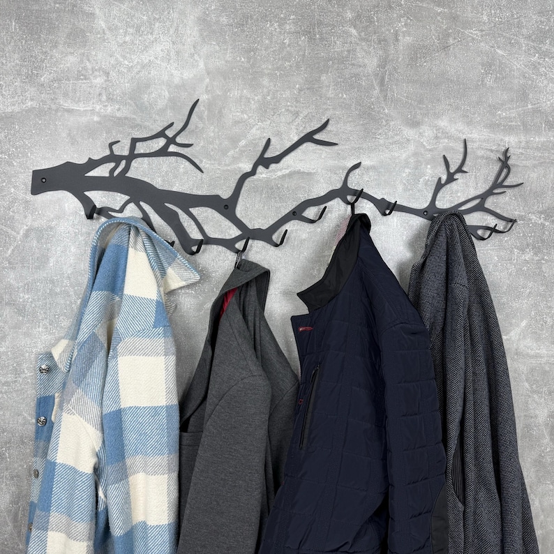 May include: A dark gray metal wall-mounted coat rack shaped like tree branches, with multiple hooks. Various coats and jackets hang from the hooks, including a blue and white plaid shirt, a gray hoodie, a navy blue quilted jacket, and a gray wool coat.