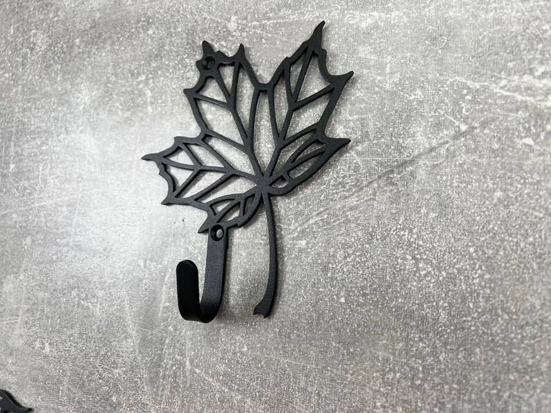 May include: Black metal wall hook shaped like a maple leaf. The hook is designed to hang items on a wall.