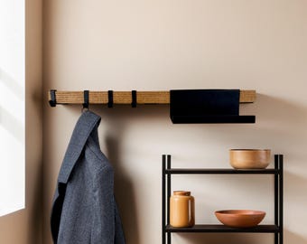 May include: A wooden coat rack with black metal hooks and a black shelf mounted on a wall. A blue coat hangs from a hook. A black metal shelf unit with wooden bowls and a ceramic jar is also visible.
