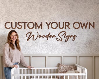 Puede incluir: Una cuna de madera blanca con una almohada blanca y una almohada estampada en su interior. En la pared sobre la cuna, letras de madera de color marrón oscuro forman el texto CUSTOM YOUR OWN Wooden Signs en letras de molde y cursiva.