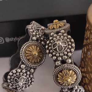 May include: Silver-toned metal bangles with gold-colored floral accents. The bangles feature a detailed design with small beads and flower-shaped embellishments. The image also shows the text "E LIFESTYLE HUB" and the Instagram handle "@style".
