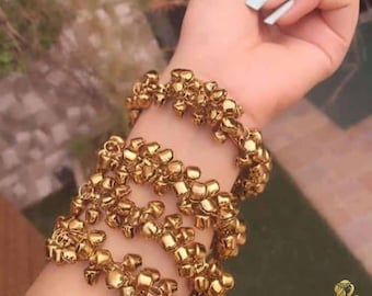 May include: Gold bangle bracelets with small bells attached. The bracelets are stacked on a person's wrist.
