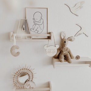 May include: A nursery room decor set with a wooden shelf, a framed print of a baby in utero, a wooden letter A, a wooden bunny rabbit toy, a wooden sign that says "Hello Little One", a wooden sign that says "Oh Boy", and a wooden sunburst mirror.