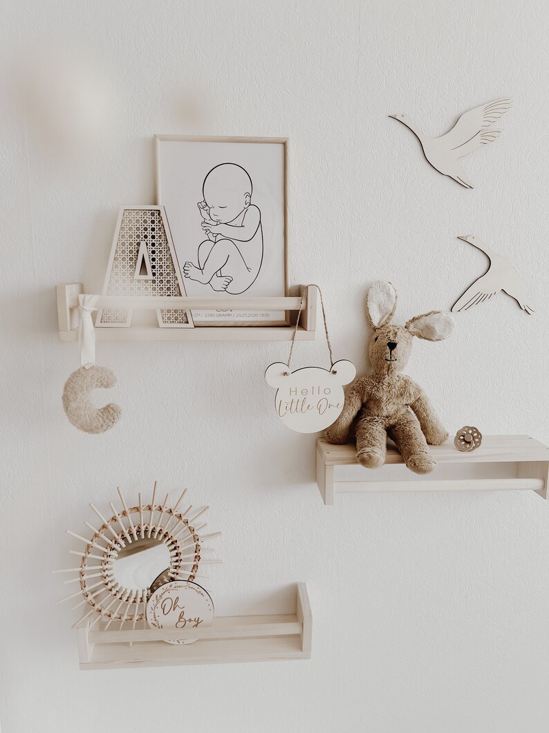 May include: A nursery room decor set with a wooden shelf, a framed print of a baby in utero, a wooden letter A, a wooden bunny rabbit toy, a wooden sign that says "Hello Little One", a wooden sign that says "Oh Boy", and a wooden sunburst mirror.