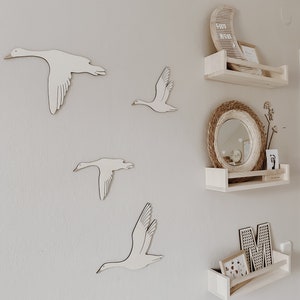 May include: A white wall with four wooden bird cutouts in the shape of geese. There are three wooden shelves with a moon-shaped sign that says "Good Night" and a round mirror with a woven frame.