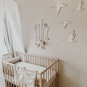 May include: A white crib with a white and black patterned sheet and a white canopy hanging above it. The wall behind the crib is beige and has wooden cutouts of birds and plants.