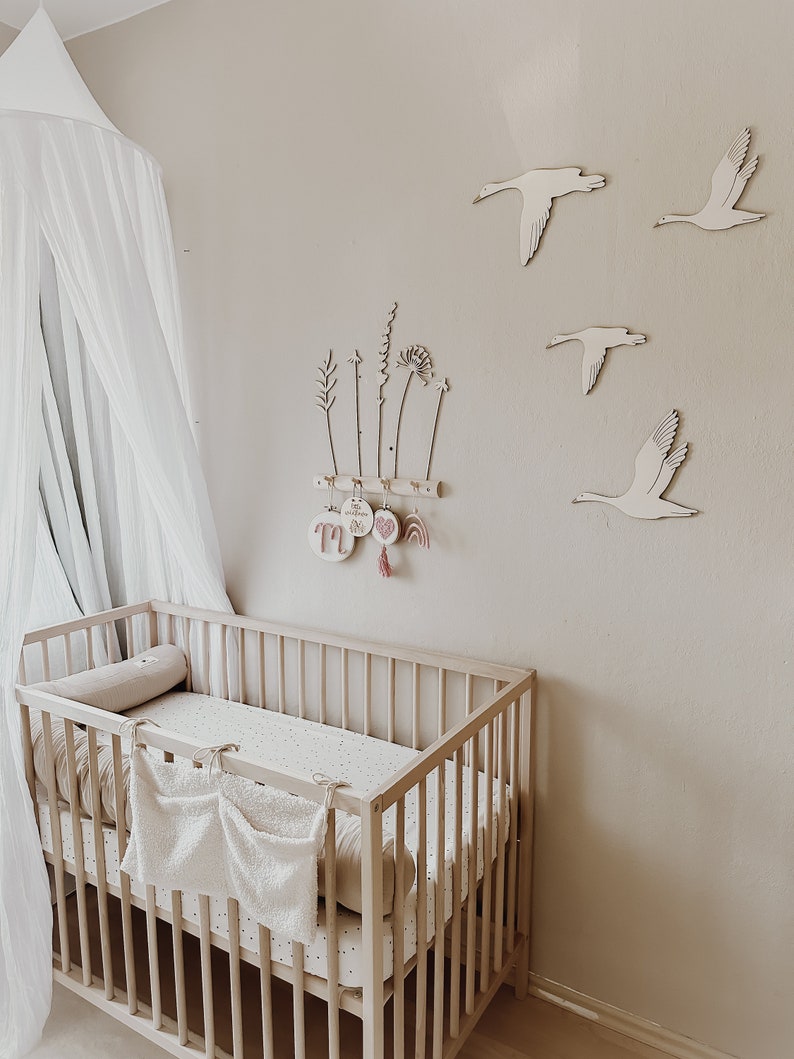 May include: A white crib with a white and black patterned sheet and a white canopy hanging above it. The wall behind the crib is beige and has wooden cutouts of birds and plants.
